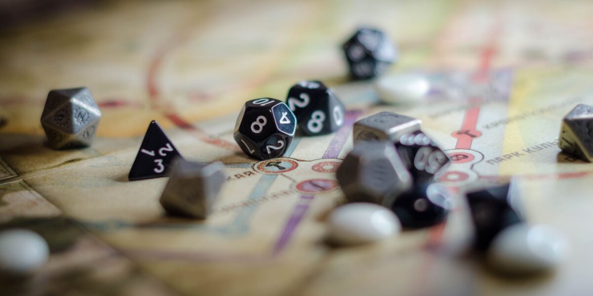 Focus on black and white polyhedral dice scattered on a board game map, suggesting strategy and chance.