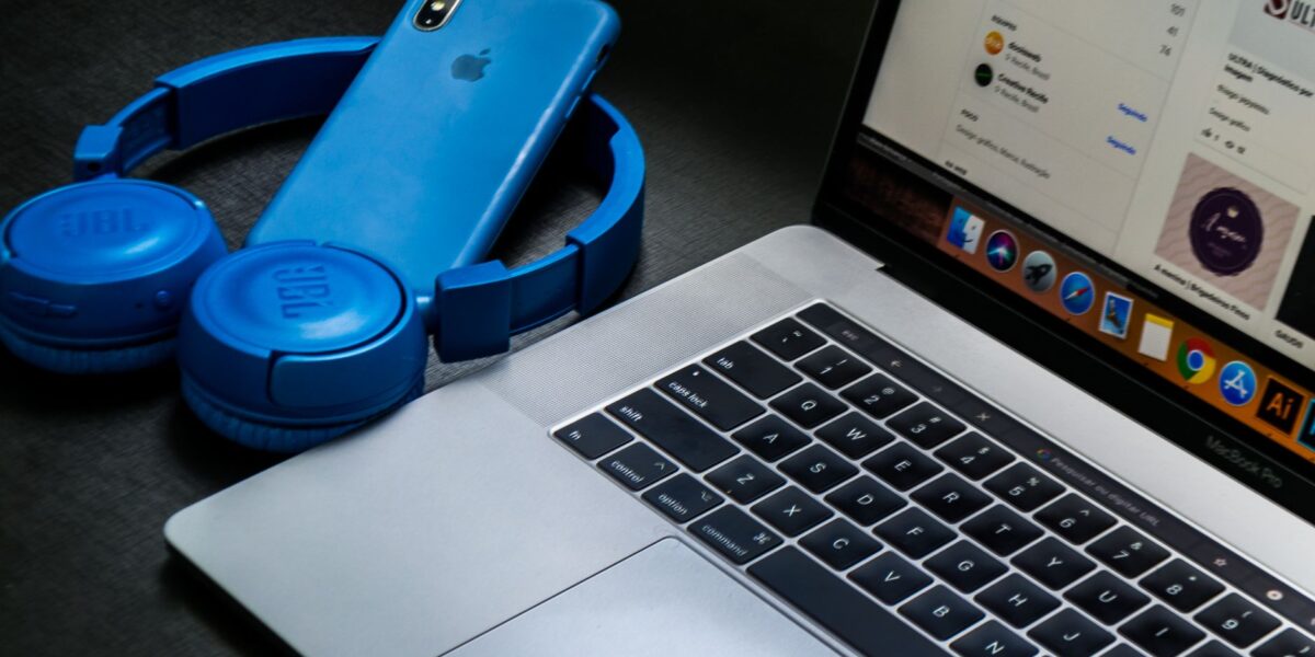 A sleek office setup featuring a laptop, blue headphones, and a smartphone, exemplifying modern technology.