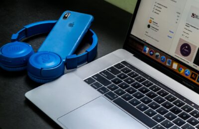 A sleek office setup featuring a laptop, blue headphones, and a smartphone, exemplifying modern technology.