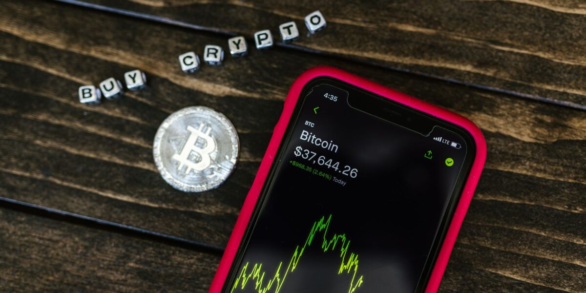 Smartphone showing bitcoin price with a physical coin and text representing cryptocurrency investment.