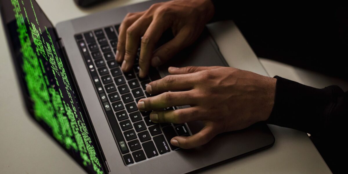 From above of crop anonymous male hacker typing on netbook with data on screen while sitting at desk