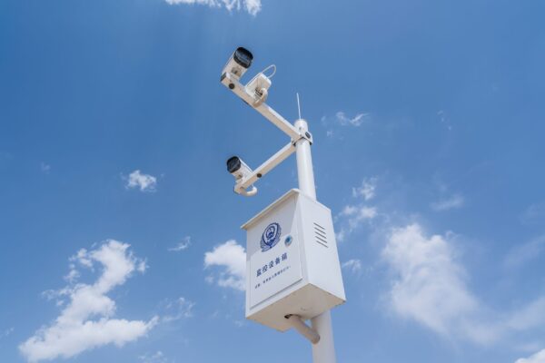 White security cameras mounted on a pole against a bright blue sky with fluffy clouds.