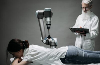 A woman receives a robotic massage as a scientist monitors, showcasing modern technology.