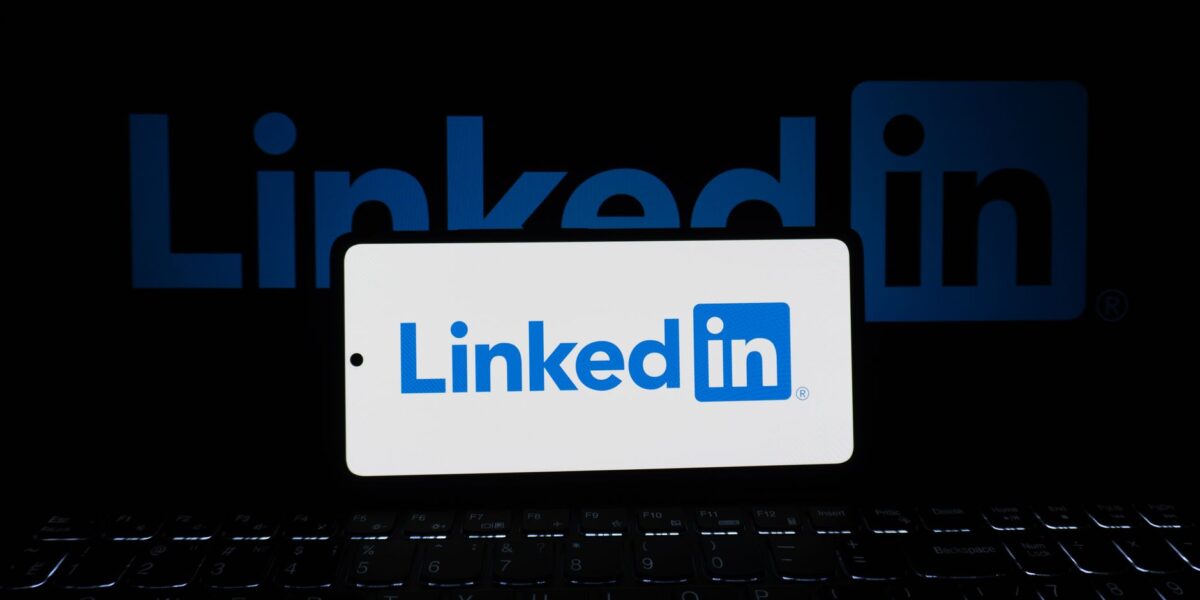 Smartphone showing LinkedIn logo with keyboard and large background logo, business theme.