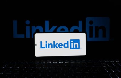 Smartphone showing LinkedIn logo with keyboard and large background logo, business theme.