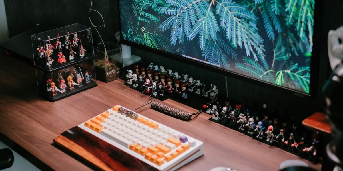 Modern desk setup featuring a custom keyboard, monitor, and collectible figurines for a tech-savvy workspace.