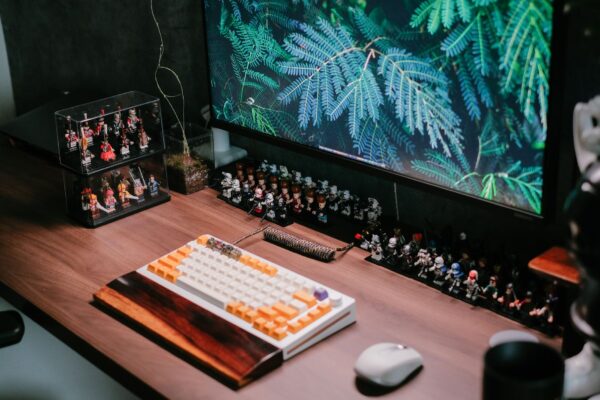 Modern desk setup featuring a custom keyboard, monitor, and collectible figurines for a tech-savvy workspace.