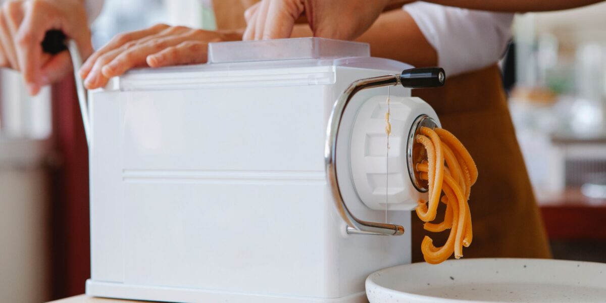 Close-up of a pasta maker producing fresh noodles in a kitchen.