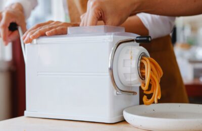 Close-up of a pasta maker producing fresh noodles in a kitchen.
