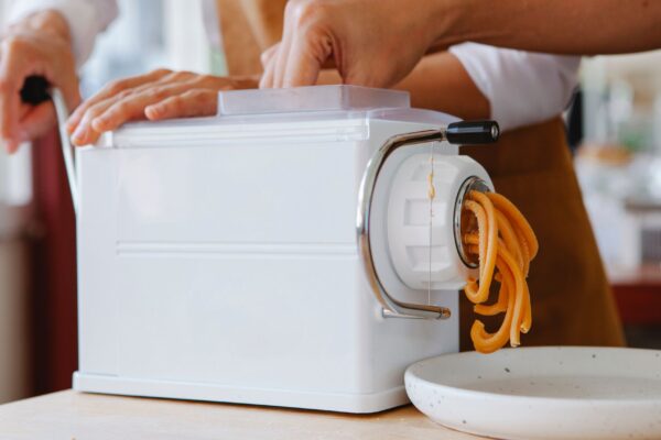 Close-up of a pasta maker producing fresh noodles in a kitchen.