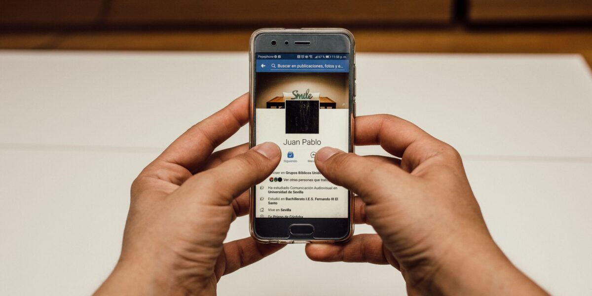 Close-up of hands using a smartphone with a social media page indoors.
