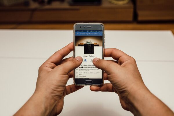 Close-up of hands using a smartphone with a social media page indoors.