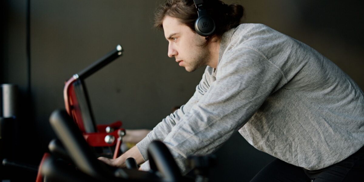 Determined young man training on exercise bike in gym, wearing headphones.