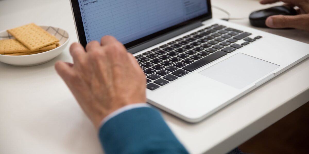 A person working on a laptop at a desk with snacks, emphasizing productivity and technology.
