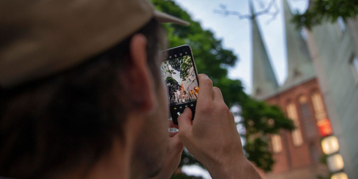 A person captures iconic Berlin church towers using a smartphone, outdoors.