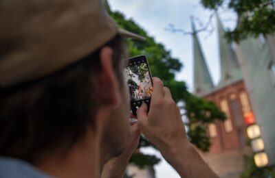 A person captures iconic Berlin church towers using a smartphone, outdoors.