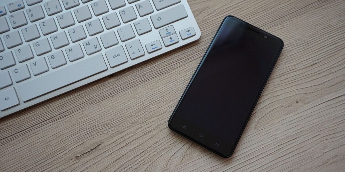 A close-up image of a keyboard and smartphone on a wooden desk, showcasing modern technology essentials.
