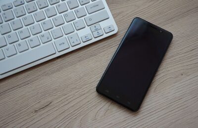 A close-up image of a keyboard and smartphone on a wooden desk, showcasing modern technology essentials.
