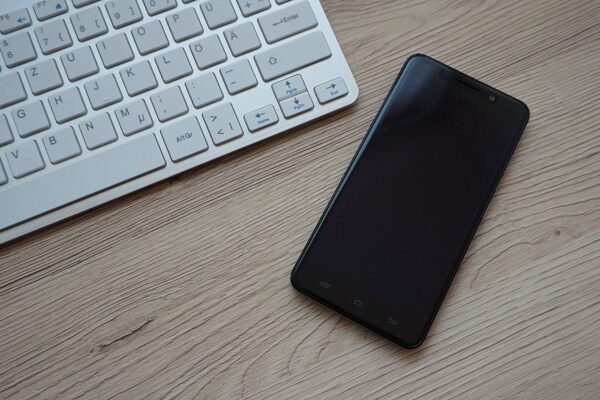 A close-up image of a keyboard and smartphone on a wooden desk, showcasing modern technology essentials.