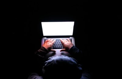 A person in a dark room typing on a laptop, symbolizing privacy, cybersecurity, and technology.