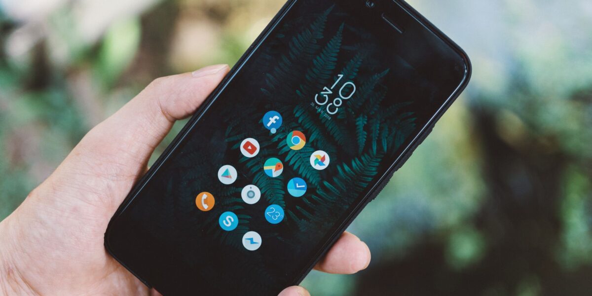 Close-up of a hand holding a smartphone with app icons and a nature wallpaper.