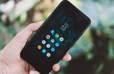 Close-up of a hand holding a smartphone with app icons and a nature wallpaper.