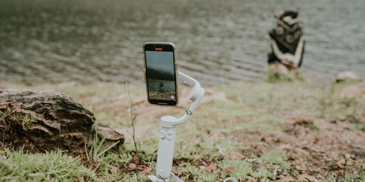 A smartphone on a gimbal capturing a tranquil lakeside scene with a person in the distance.