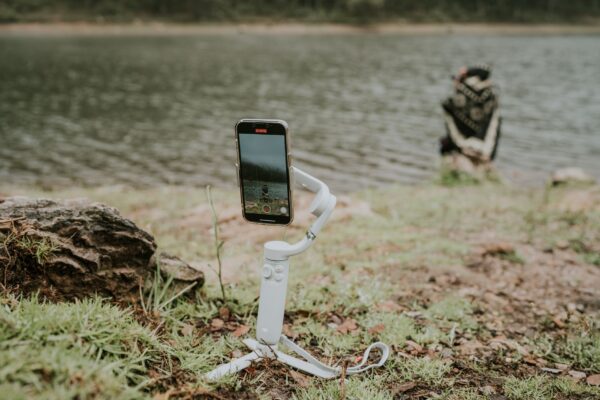 A smartphone on a gimbal capturing a tranquil lakeside scene with a person in the distance.