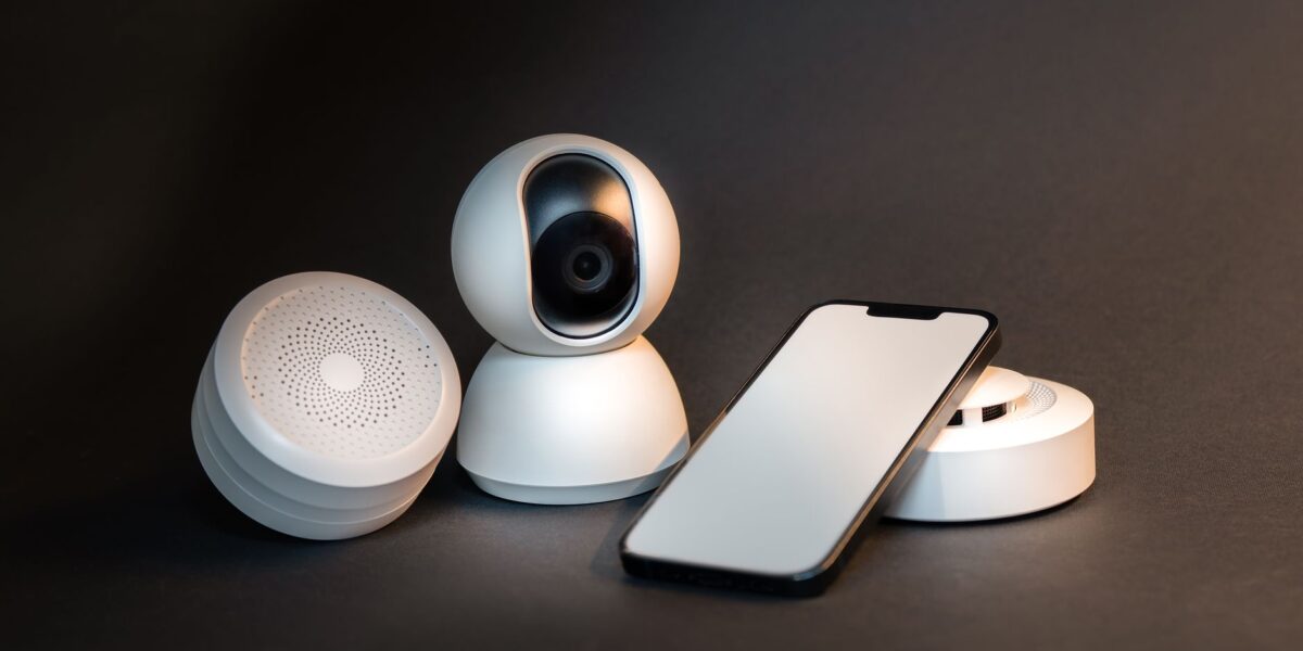 A sleek smartphone with modern smart home devices on a minimalist gray background.