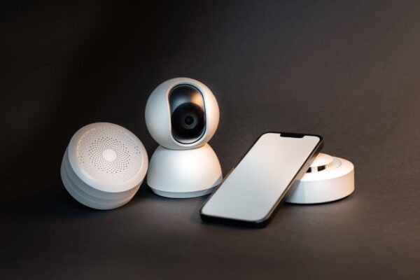 A sleek smartphone with modern smart home devices on a minimalist gray background.
