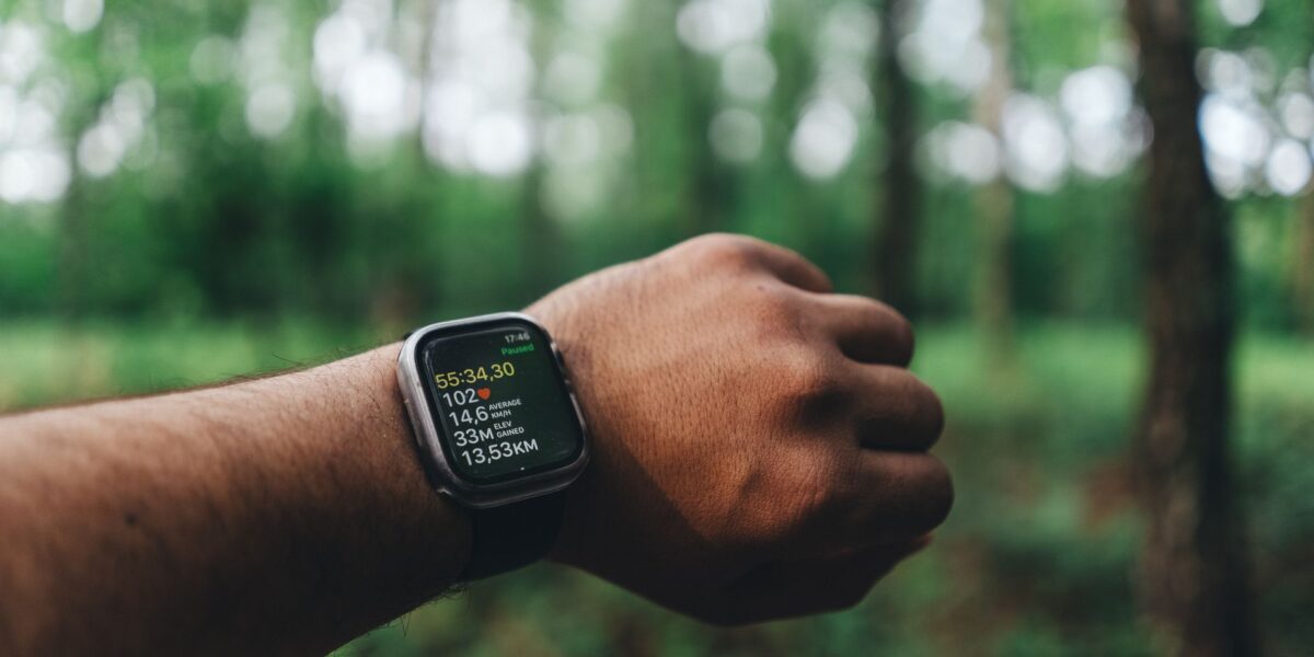 Close-up of a hand wearing a smartwatch with blurred forest background, showing fitness metrics.