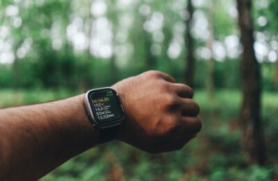 Close-up of a hand wearing a smartwatch with blurred forest background, showing fitness metrics.