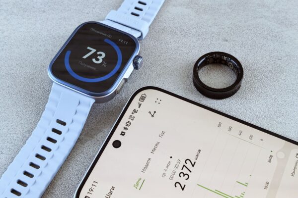 Smartwatch with fitness data, smartphone, and health ring on a gray surface.