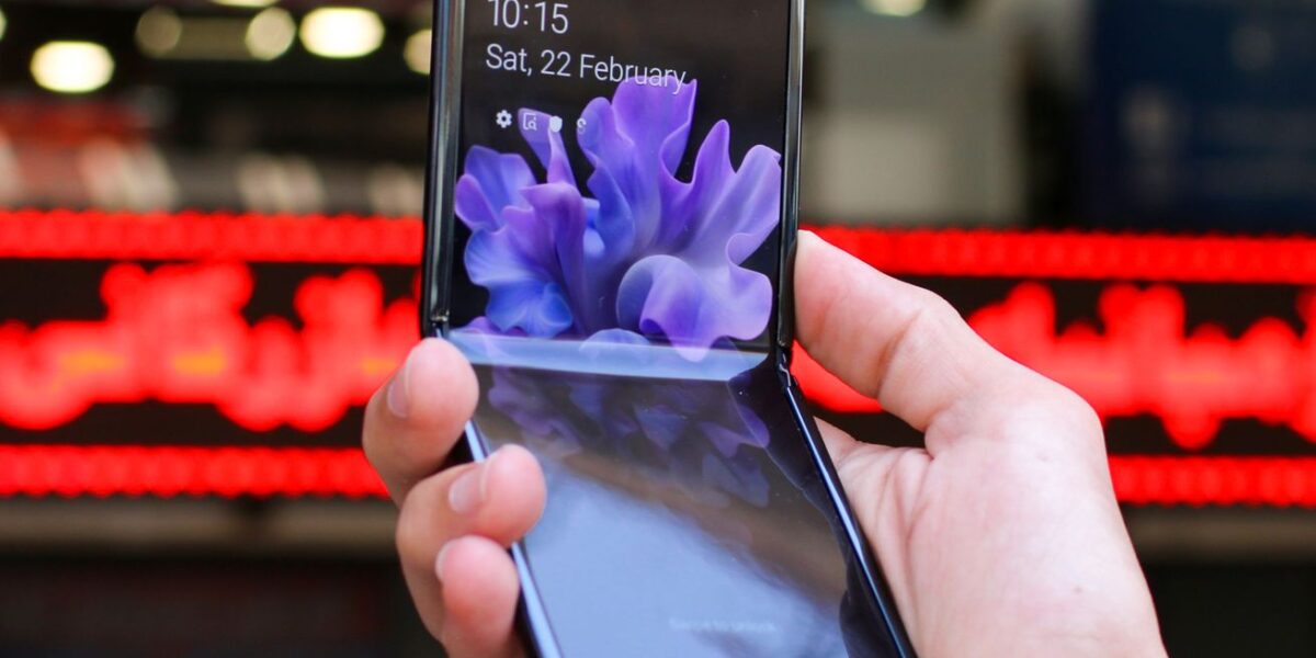 Close-up of a modern flip smartphone held in hand, showcasing innovative technology outdoors in a bustling city.