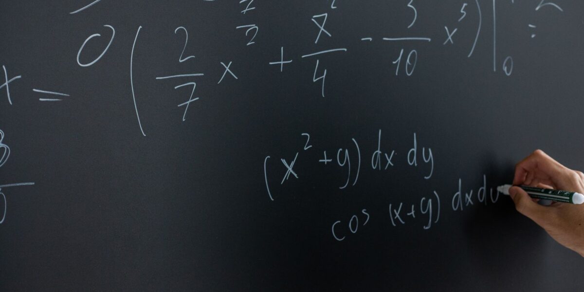 Hand writing mathematical equations on a chalkboard in a classroom setting.