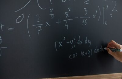 Hand writing mathematical equations on a chalkboard in a classroom setting.