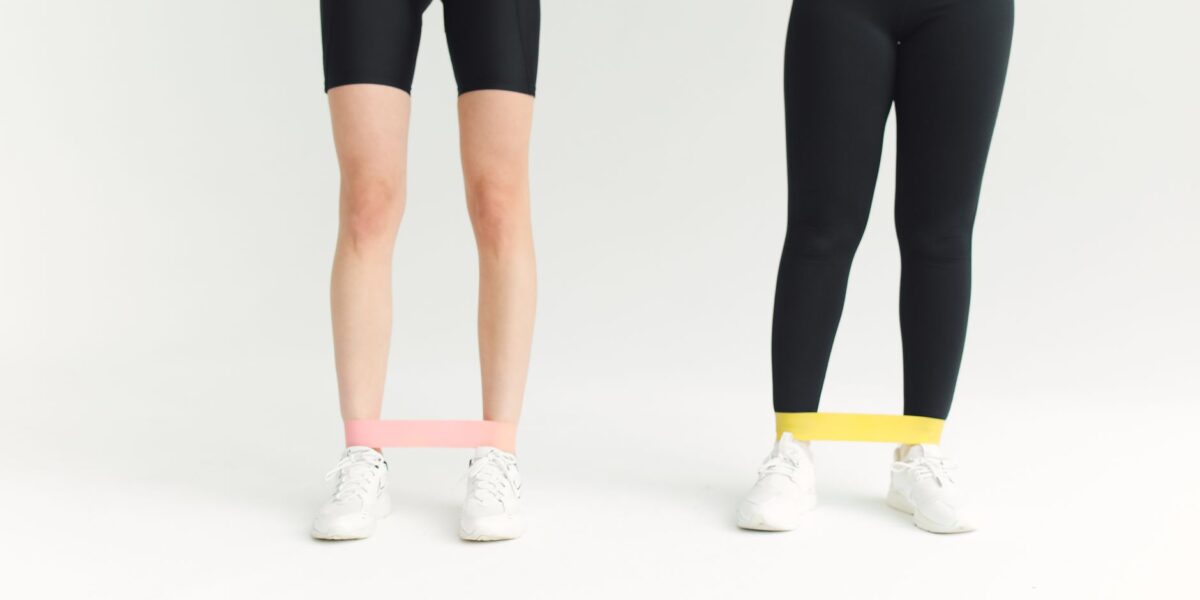 Two women in activewear using resistance bands during an indoor workout session.