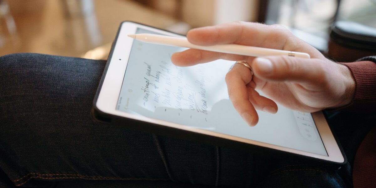 Close-up of a hand holding a stylus, writing on a tablet, featuring handwritten notes. Ideal for digital creativity concepts.