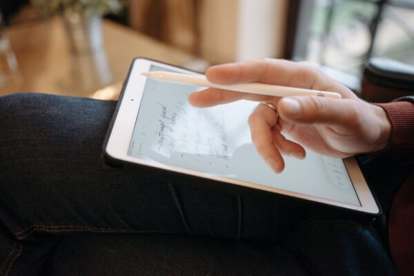 Close-up of a hand holding a stylus, writing on a tablet, featuring handwritten notes. Ideal for digital creativity concepts.