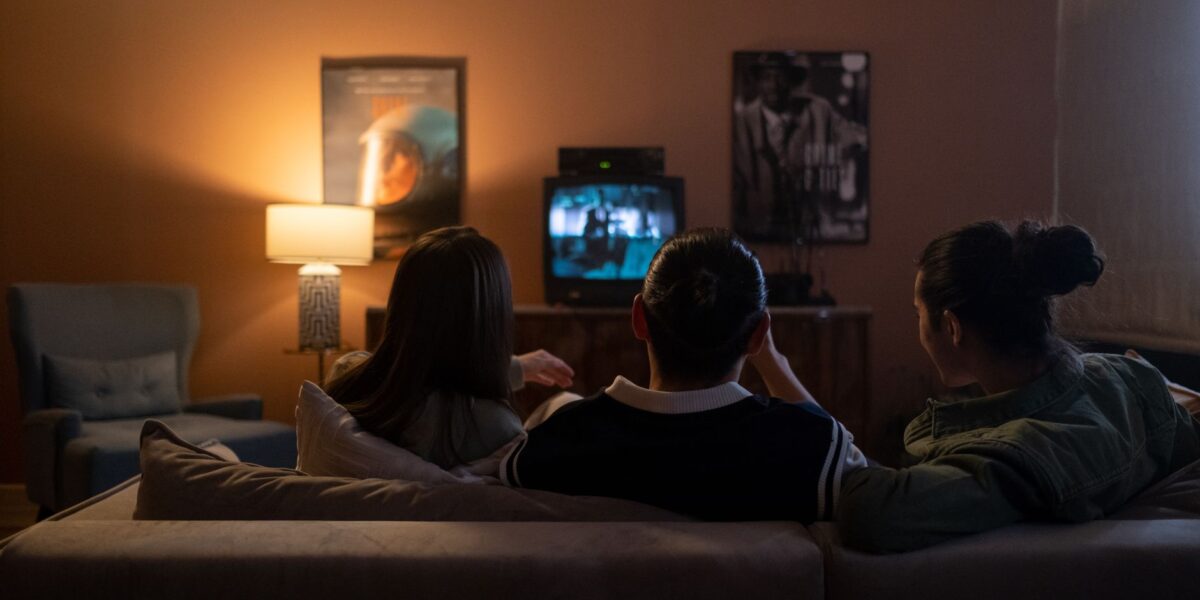 Three people enjoying a relaxed movie night at home, sitting on a couch in a cozy living room.