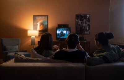 Three people enjoying a relaxed movie night at home, sitting on a couch in a cozy living room.