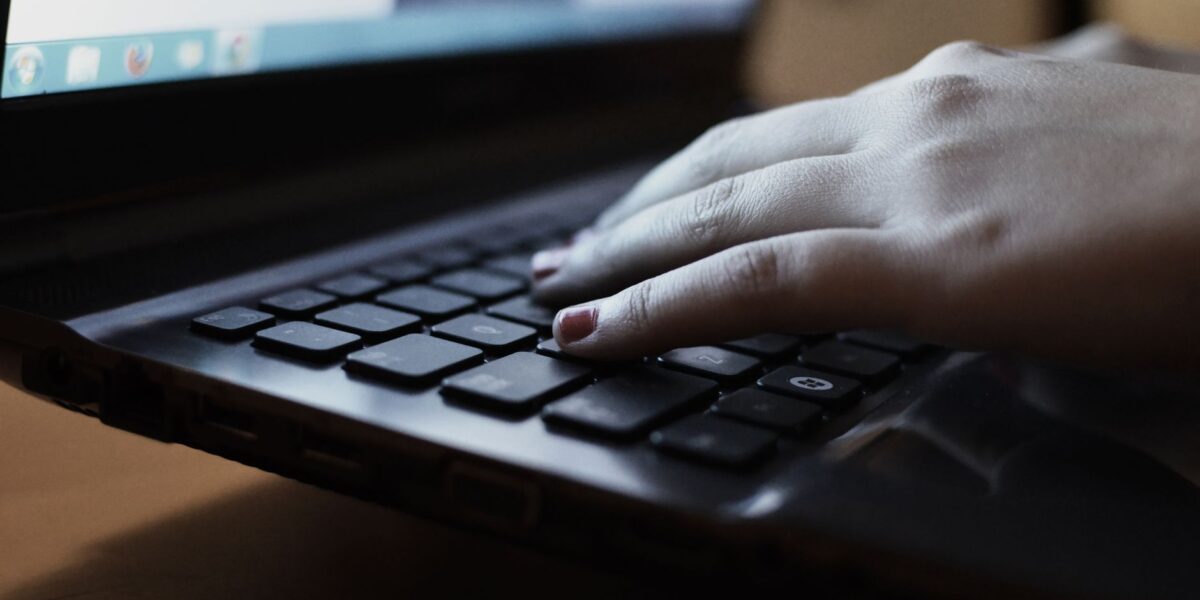 A close-up view of a person typing on a laptop keyboard indoors.
