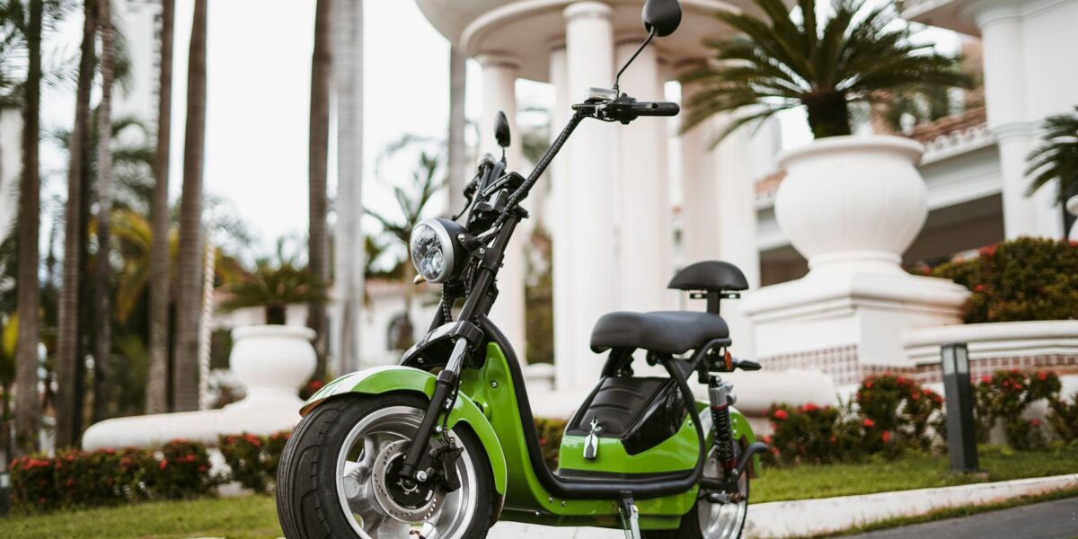 A stylish green electric moped parked in an outdoor urban setting during the day.