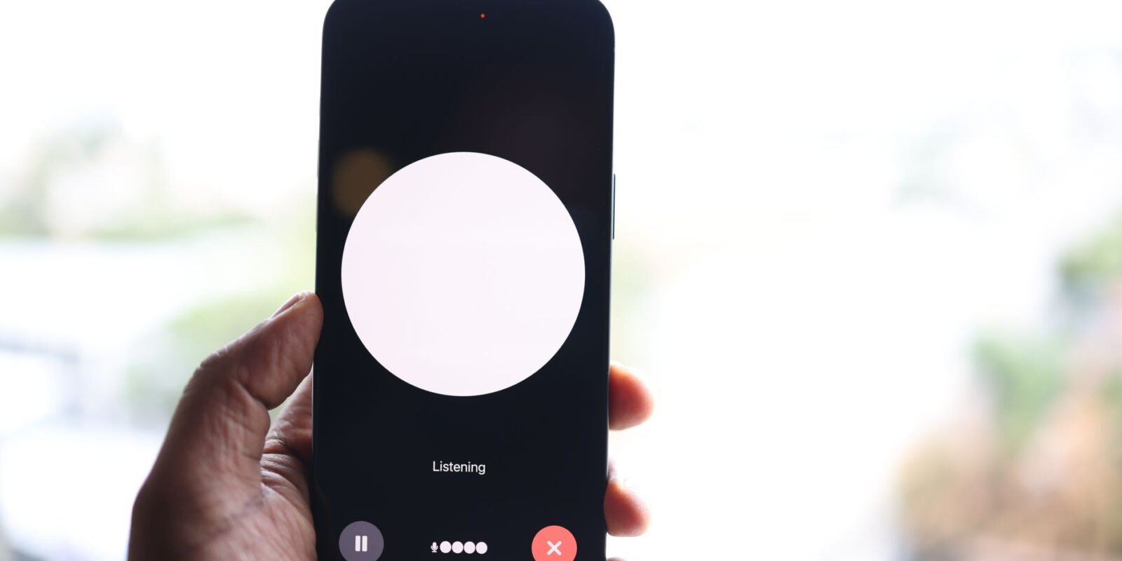Close-up of a hand holding a smartphone displaying a voice assistant interface.