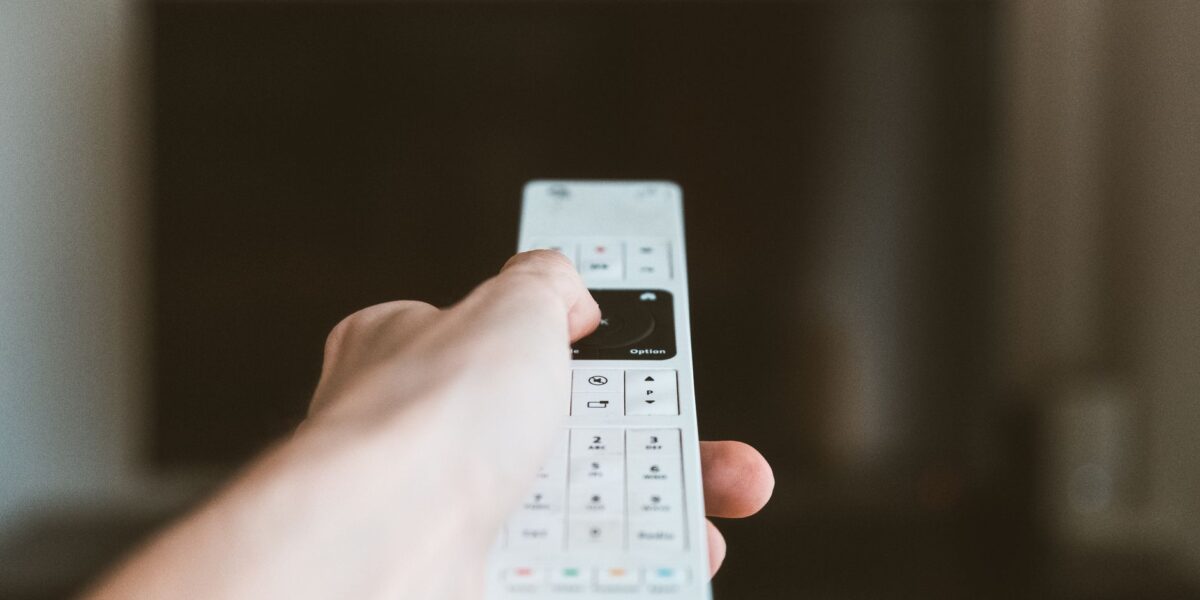 Close-up of a hand using a remote control to operate a television indoors.