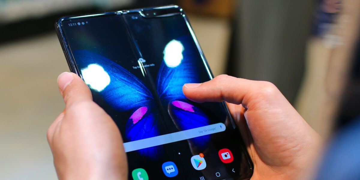 Close-up of hands holding a foldable smartphone showing a butterfly on the screen.