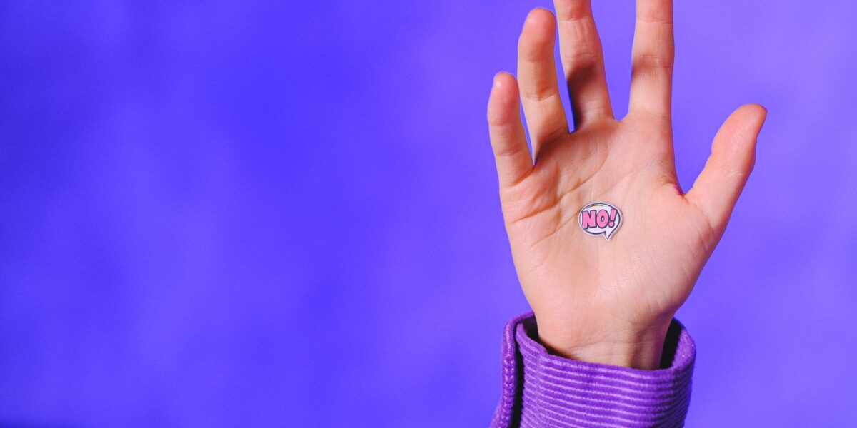 Crop unrecognizable person demonstrating small sticker with word No placed on raised hand against blue background