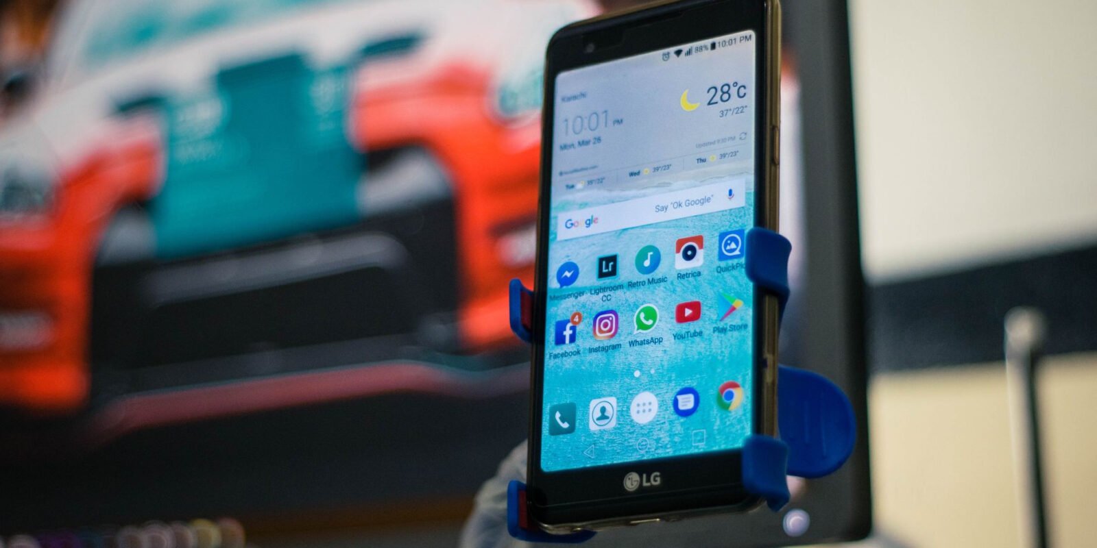 LG smartphone securely mounted in a car holder indoors, displaying various apps on the screen.