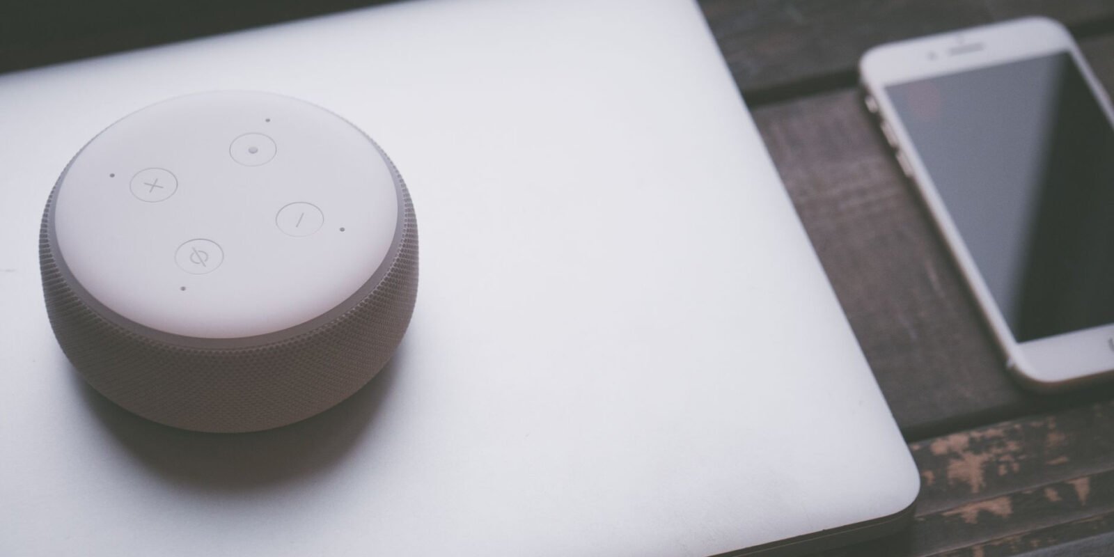 A smart speaker, laptop, and smartphone array representing modern technology lifestyle on a wooden surface.