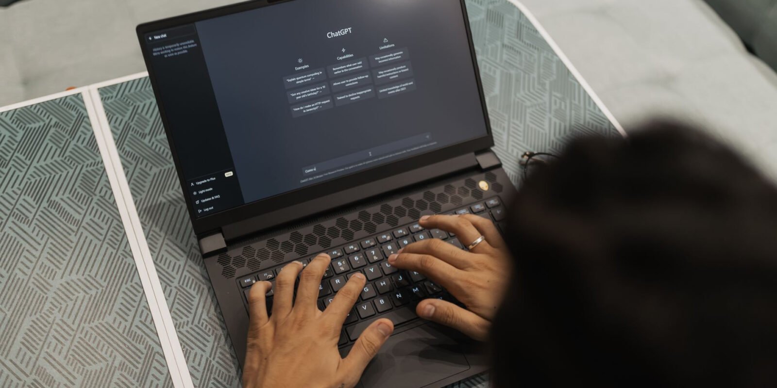 Close-up of hands typing on a laptop displaying ChatGPT interface indoors.